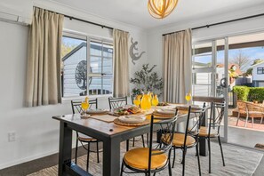 A dining area with a table set for four, chairs, and a large window with curtains. - Cosy Corner on Macdonell (Taupo)