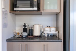 Une petite cuisine équipée d’un four à micro-ondes, d’une machine à café, ainsi que de récipients pour le sucre et le café.