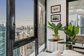 A modern room with a large window, a potted plant, a framed picture, and a small table. - 36th Floor Luxury 2BR City Views Pool & 2 Cars (Southbank)