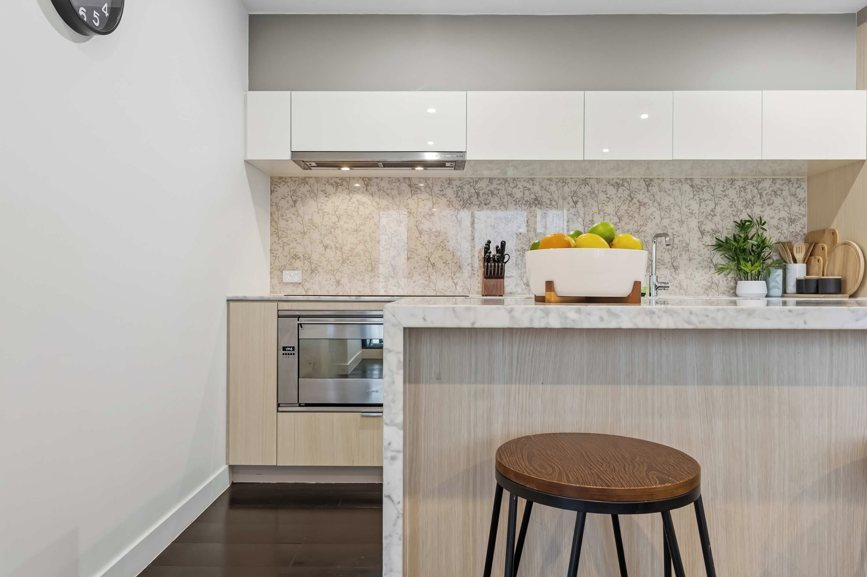 A modern kitchen with a built-in oven, a marble backsplash, and a wooden island with a bowl of fruit.