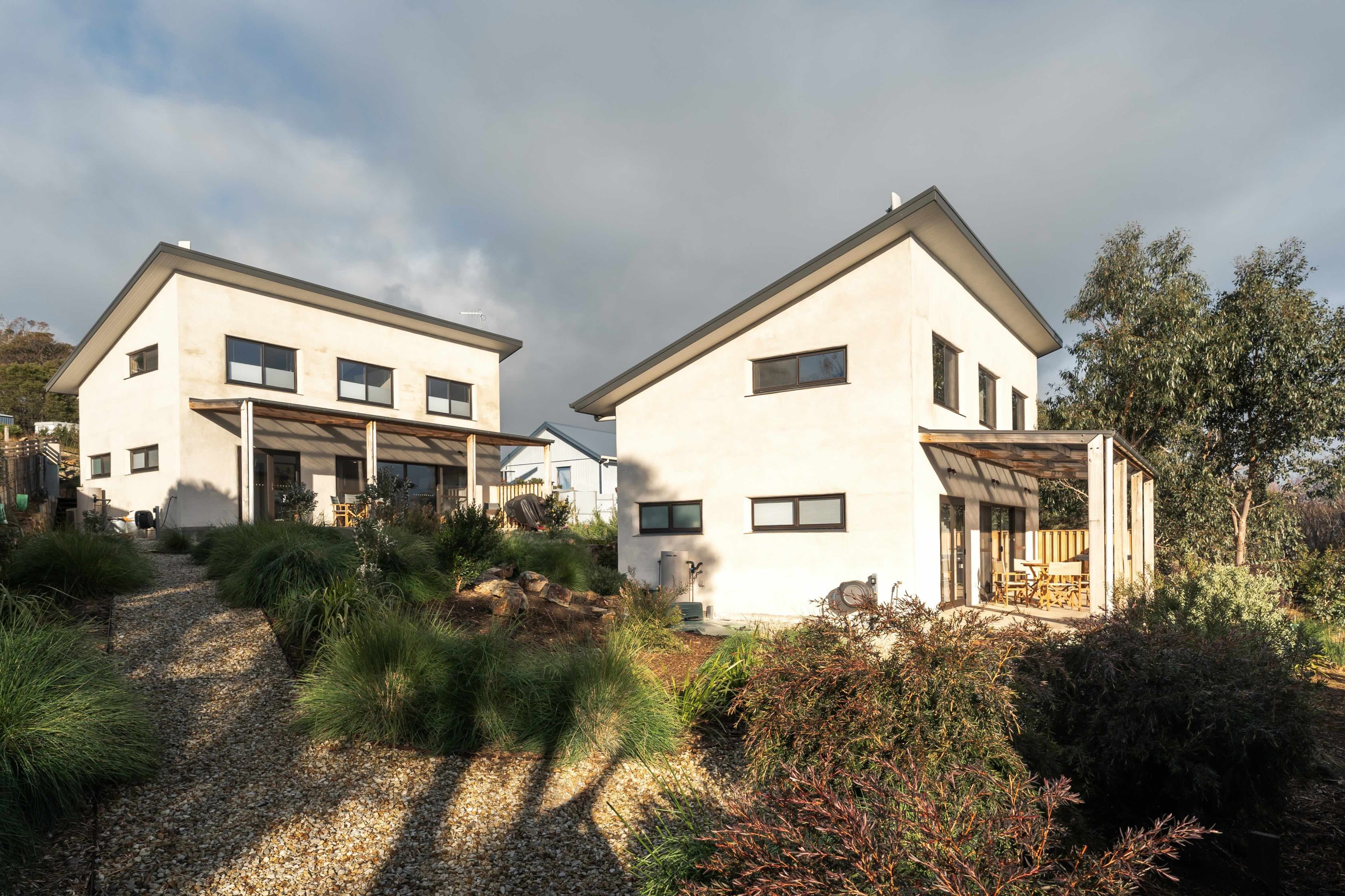 Une maison moderne à deux étages, dotée d’un toit en pente, de grandes fenêtres et d’un espace extérieur aménagé avec un coin salon abrité.