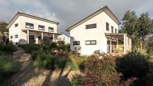 Une maison moderne à deux étages, dotée d’un toit en pente, de grandes fenêtres et d’un espace extérieur aménagé avec un coin salon abrité.