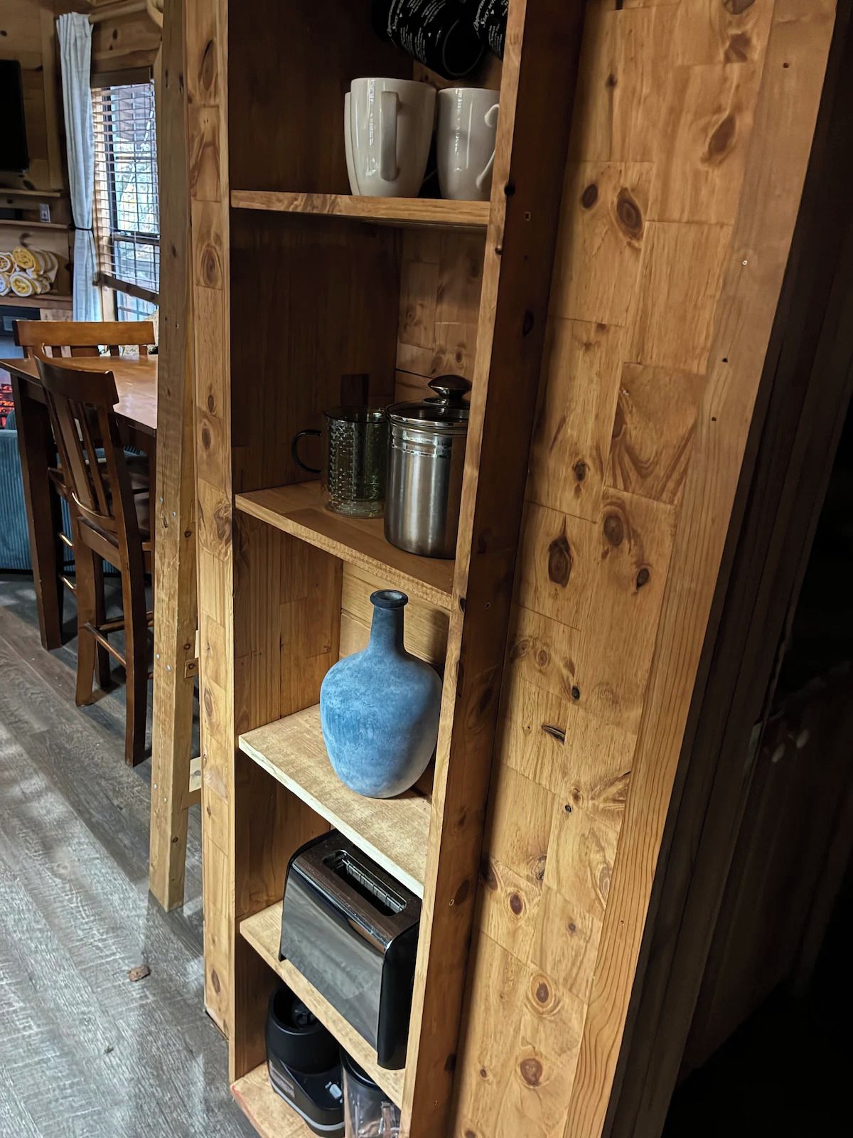 Un estante de madera con utensilios de cocina, un florero azul y una tostadora.