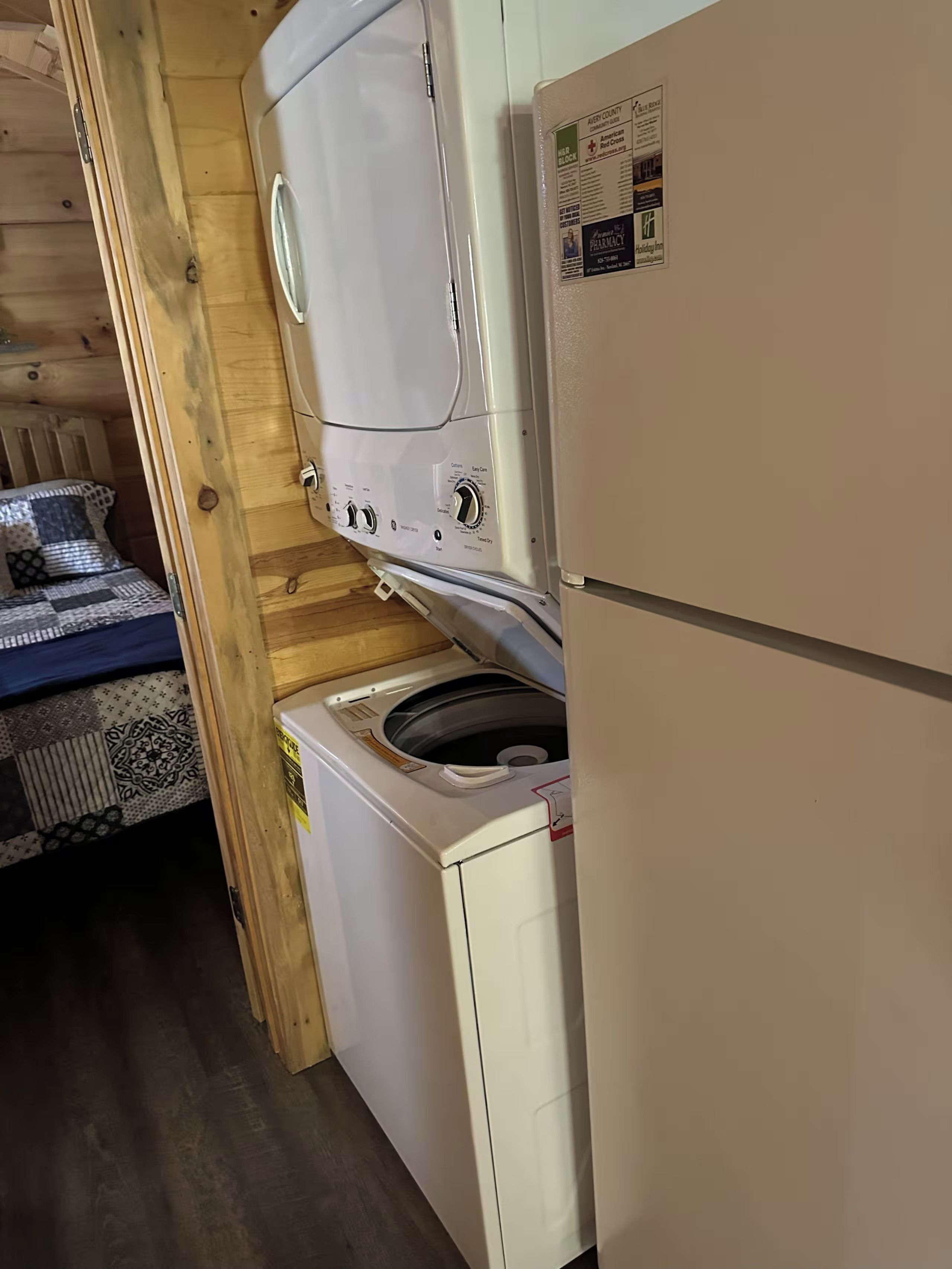 Une petite pièce équipée d’un lave-linge, d’un réfrigérateur et d’un lit avec une literie à motifs.