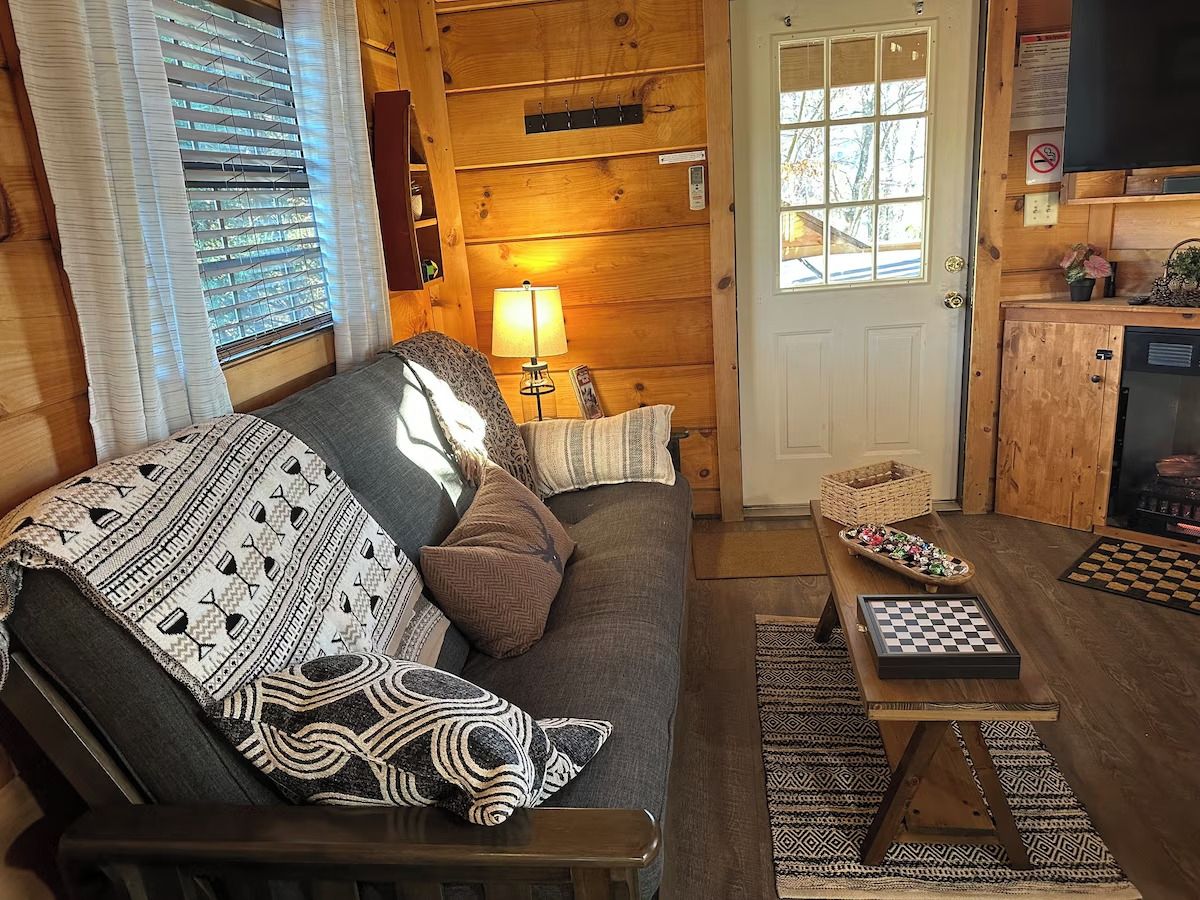 A cozy cabin interior with a sofa, a lamp, a checkered table, and a wooden door.