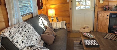A cozy cabin interior with a sofa, a lamp, a checkered table, and a wooden door.