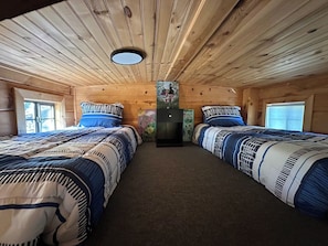 Quarto estilo cabana com duas camas, uma mesinha e um refrigerador.