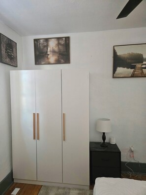 A bedroom with a wardrobe, a bedside table with a lamp, and two framed pictures on the wall.