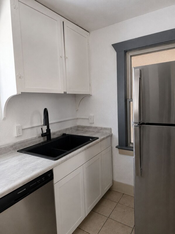 A kitchen with white cabinets, a black sink, a stainless steel refrigerator, and a window with a dark frame.