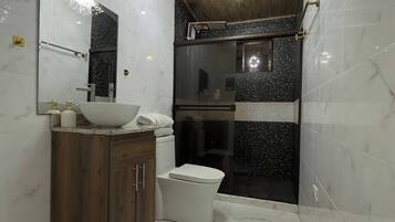 A modern bathroom with a wooden ceiling, a freestanding sink, a toilet, and a shower enclosure.