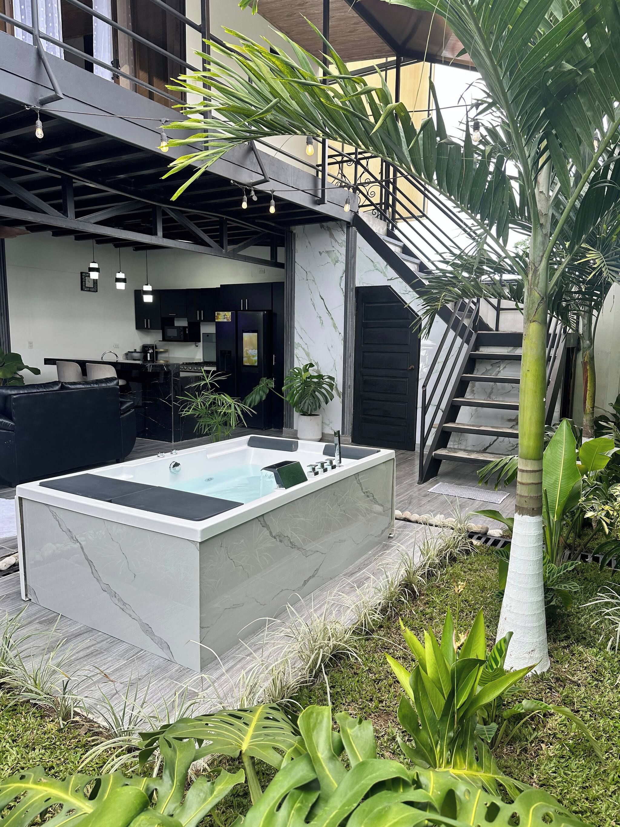 A modern outdoor area with a spa tub, staircase, and kitchen area.