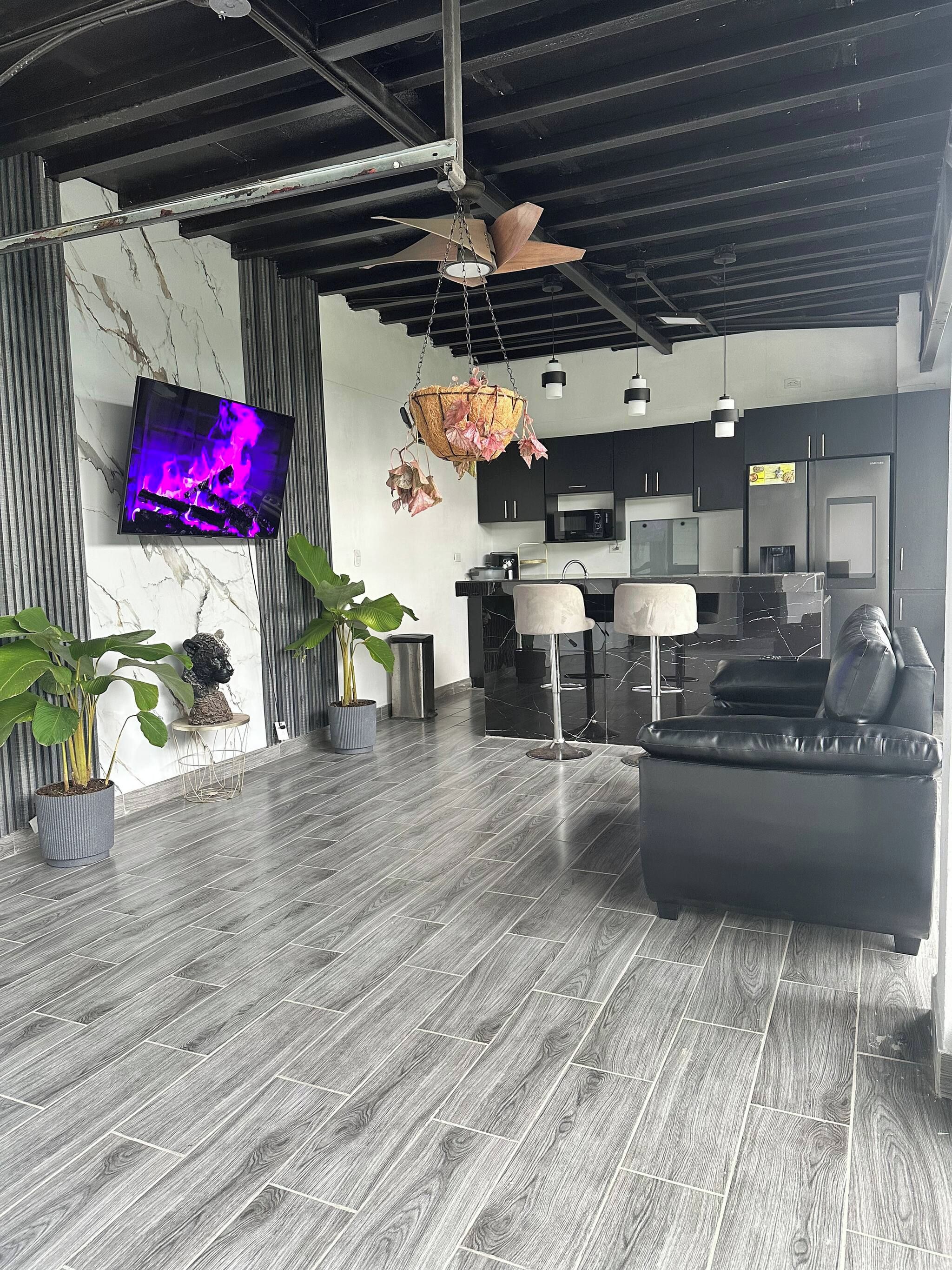 A modern living room with a flat-screen TV, a black leather sofa, and a hanging light fixture.
