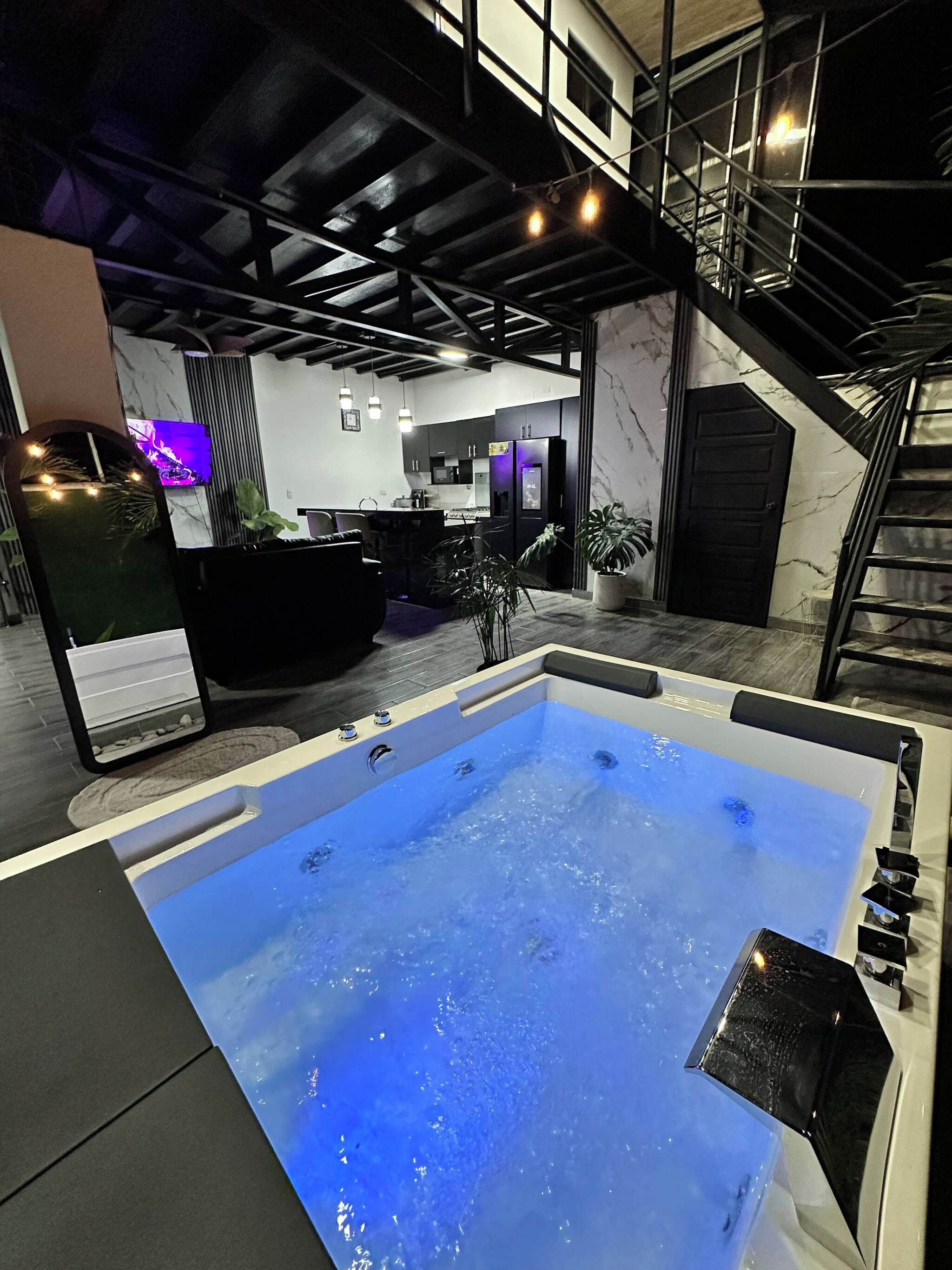 A modern interior with a hot tub, a kitchen area, and a staircase.