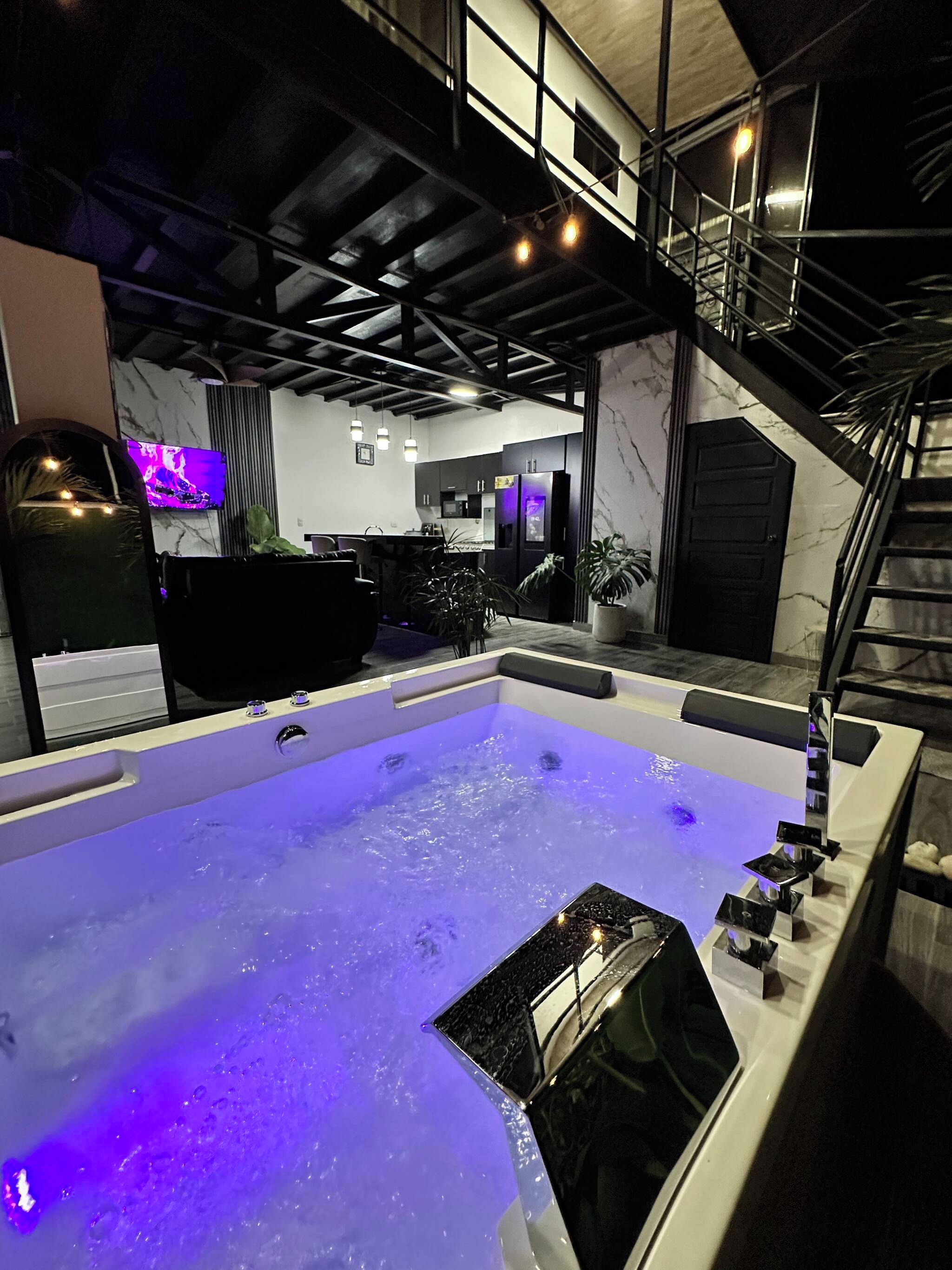A modern interior with a large hot tub, a staircase, and a kitchen area.