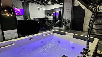 A modern interior with a large hot tub, a staircase, and a kitchen area.