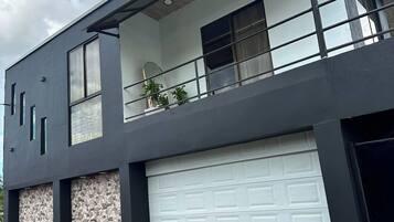 A modern two-story house with a garage, stone facade, and a balcony with plants.