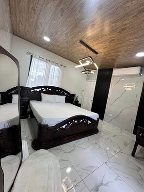 A bedroom with a wooden ceiling, a bed with a headboard, a bedside table, a mirror, a window with curtains, and a wall-mounted air conditioner. - Betandy Apartment Jacuzzi (Rita)
