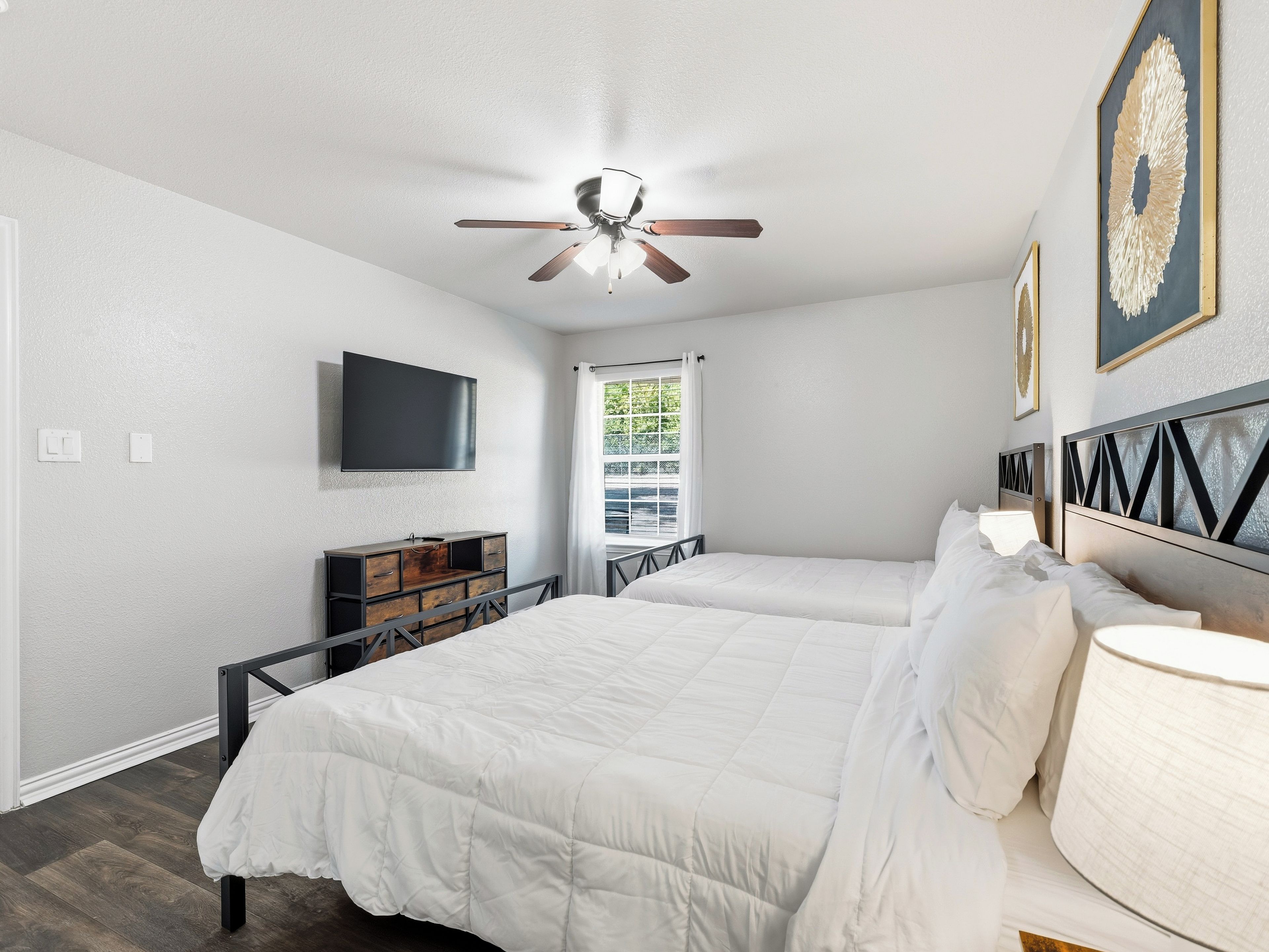 Une chambre avec deux lits, un ventilateur de plafond, une télévision et une fenêtre avec des rideaux.