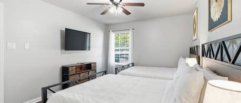 A bedroom with two beds, a ceiling fan, a TV, and a window with curtains.