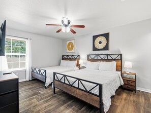A hotel room with two beds, a ceiling fan, artwork on the walls, and a window with blinds. - Walk to Games! AT&T & Globe Life! Free Parking! (Arlington)