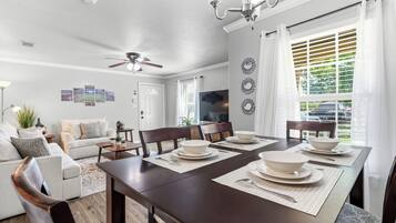 Un coin repas avec une table en bois foncé, dressée pour quatre personnes, un ventilateur de plafond et un téléviseur fixé au mur.