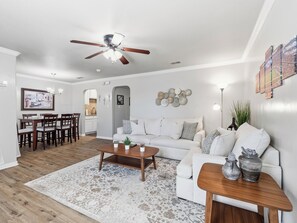 A modern living room with a white sofa, wooden coffee table, and a dining area with a white table and chairs. - Walk to Games! AT&T & Globe Life! Free Parking! (Arlington)