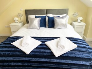 A neatly made bed with a striped bedspread, two pillows, and two folded towels. - Modern 4-Bed House | Windsor | Driveway + Garden (Windsor)