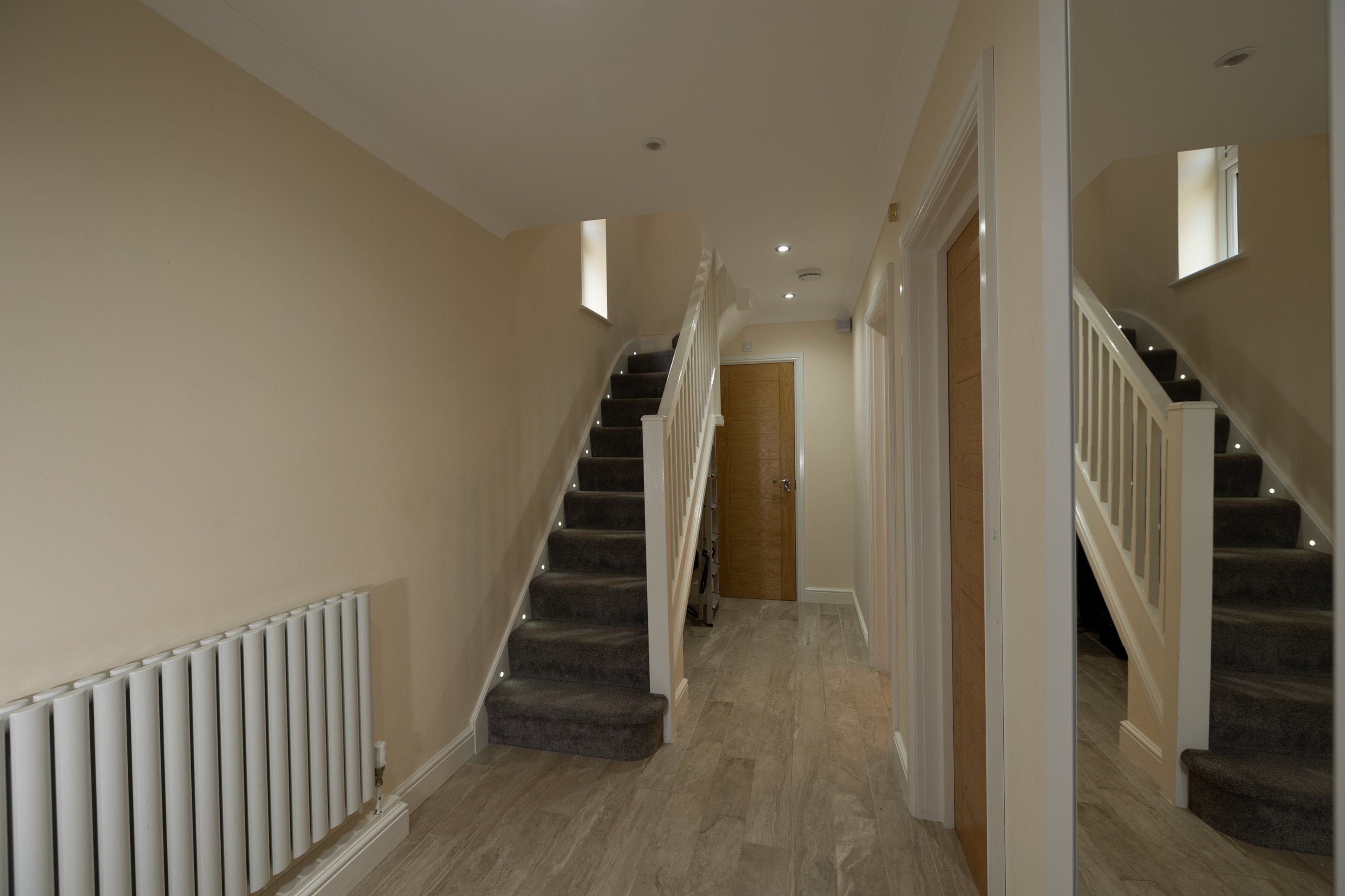 A hallway with carpeted stairs, a radiator, and a wooden door at the end.