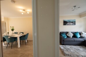 Een eetgedeelte met een tafel voor vier personen, een bank met decoratieve kussens en een schilderij aan de muur.