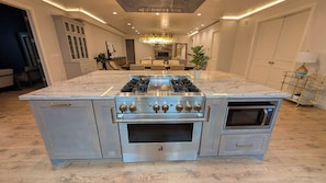 Cozinha com ilha central, eletrodomésticos de aço inoxidável e um candelabro.