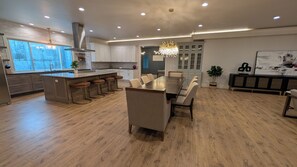 Cozinha moderna com ilha central, banquetas, mesa de jantar com cadeiras e um candelabro.