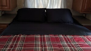 Un dormitori amb un llit, armaris de fusta i una finestra amb cortines.