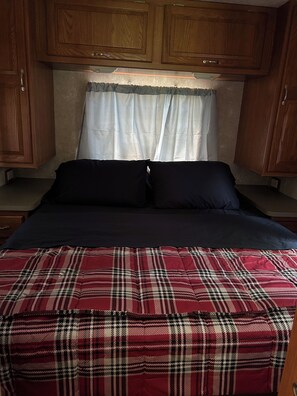 A bedroom with a bed, wooden cabinets, and a window with curtains. - RV Retreat near Chemung River (Elmira)