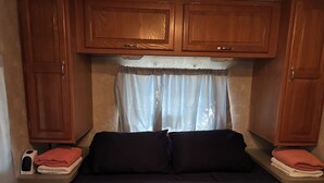 Habitació compacta amb llit, armaris de fusta, finestra amb cortines i taula de nit amb telèfon i tovalloles.
