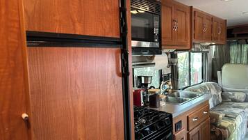 A compact RV kitchen with a stove, microwave, and wooden cabinets.