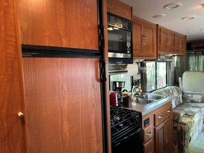 A compact RV kitchen with a stove, microwave, and wooden cabinets.