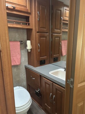 A compact bathroom with wooden cabinets, a white toilet, a sink, and a towel rack. - RV Retreat near Chemung River (Elmira)