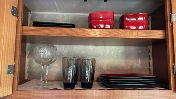 Un meuble en bois doté d’étagères contenant des récipients noirs et rouges, un verre à vin et deux verres transparents.