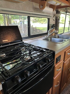 A kitchen with a stove, sink, and wooden cabinets.
