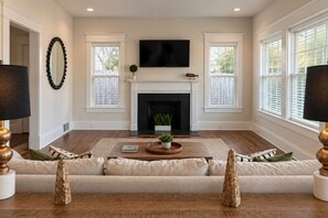 A living room with a fireplace, a television mounted above it, and a sofa with decorative vases. - The Historic House (Dothan)