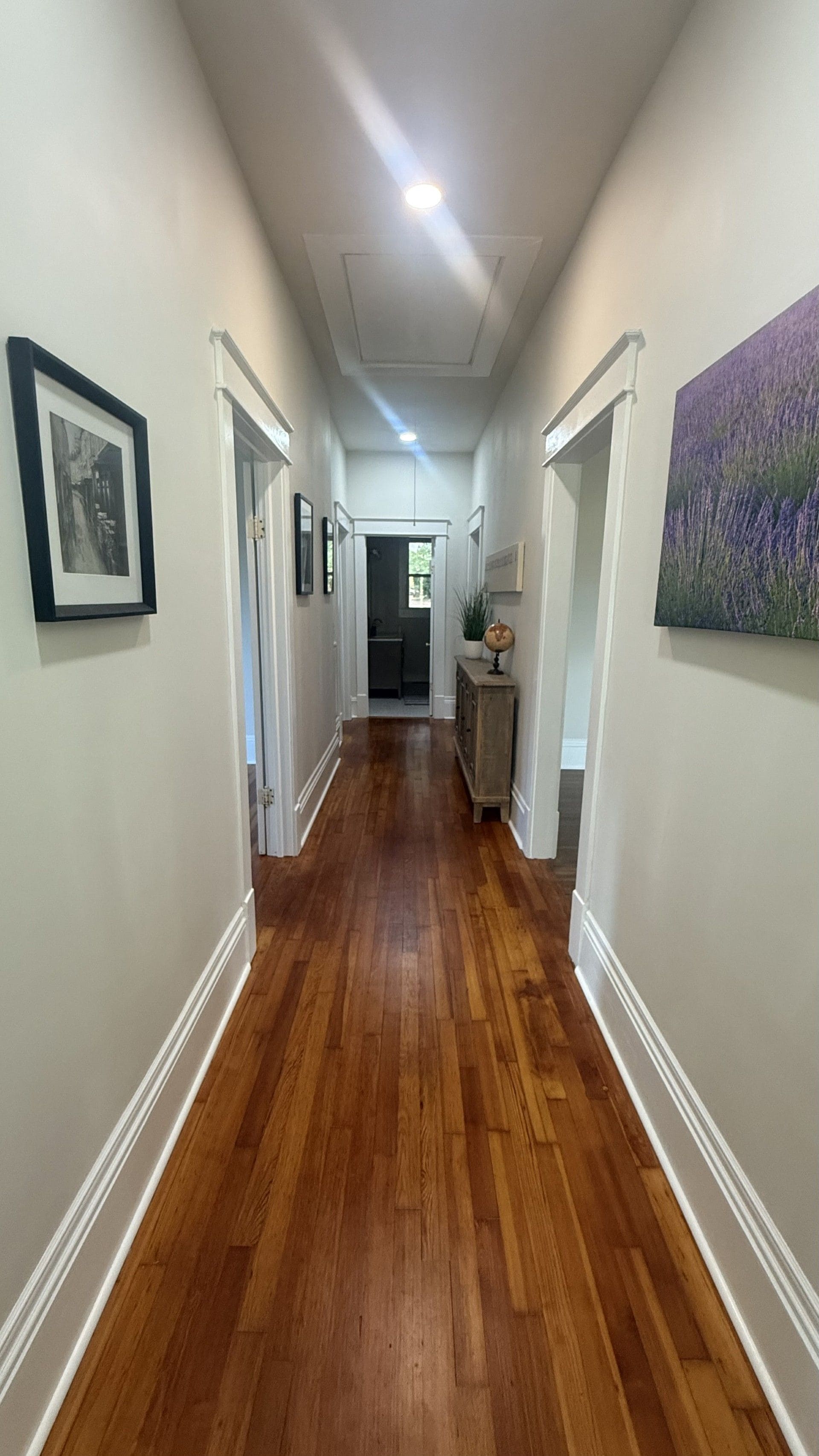 A hallway with wooden flooring, white walls, and framed pictures.