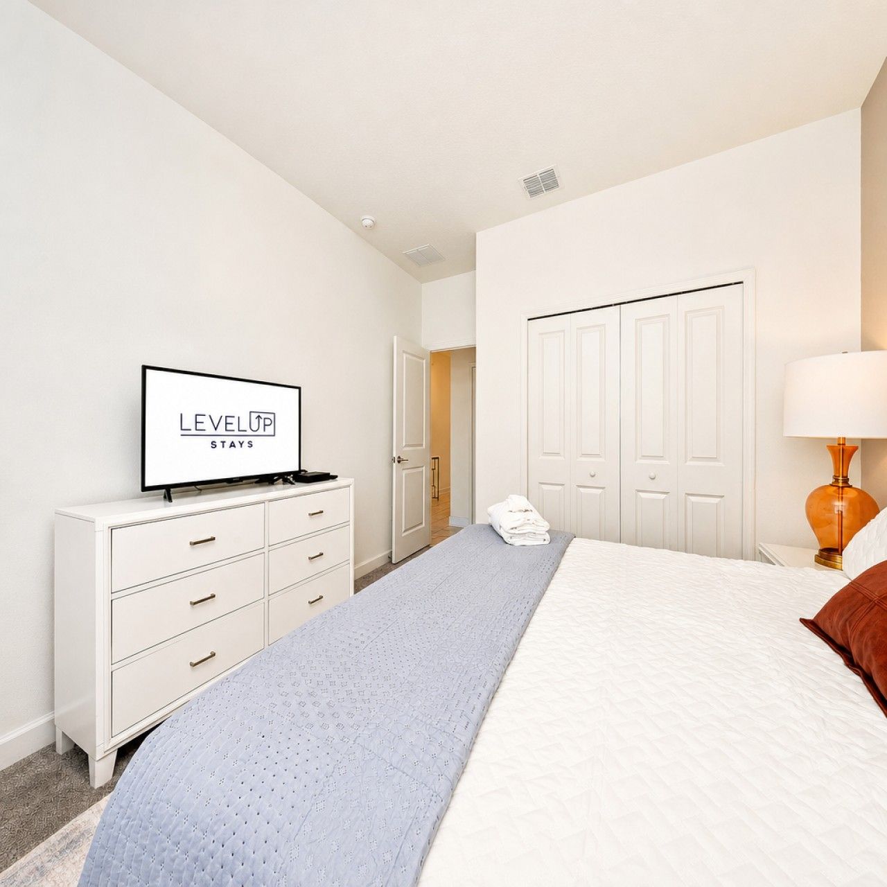 A hotel room with a bed, a TV on a dresser, a lamp, and a wardrobe.