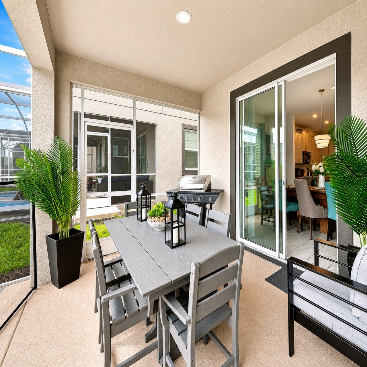 An outdoor patio with a dining table, chairs, a grill, and potted plants.