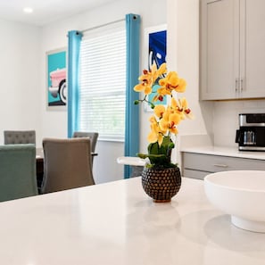 Eine moderne Küche mit weißer Arbeitsplatte, einer dekorativen Schale mit gelben Orchideen und einem Essbereich mit Stühlen und Tisch.
