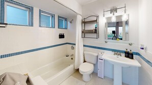 A bathroom with a bathtub, toilet, and sink. There are windows with blue-tiled frames and a mirror with lights above the sink. - A little retreat in Seattle perfect for your next getaway (Seattle)