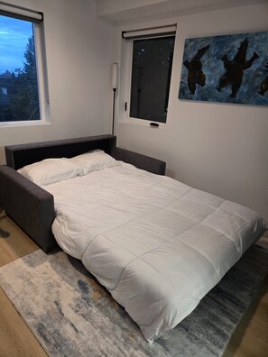 Ett modernt sovrum med en säng, ett fönster och en tavla på väggen.