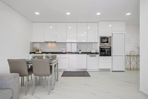 A modern kitchen with white cabinetry, a dining area with chairs, and a built-in oven. - CableCar House I, by Pausa Vacation Rentals (Câmara de Lobos)