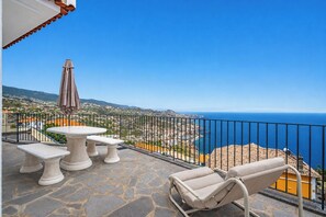 A terrace with a table and chairs, a view of the sea, and a mountainous landscape. - CableCar House I, by Pausa Vacation Rentals (Câmara de Lobos)