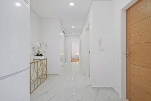 A hallway with a marble floor, a wooden door, and a white console table with a plant. - CableCar House I, by Pausa Vacation Rentals (Câmara de Lobos)