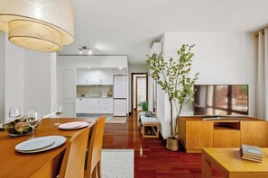 Ein modernes Wohnzimmer mit einem Couchtisch aus Holz, einer TV-Konsole und einem Essbereich mit Holztisch und Stühlen.